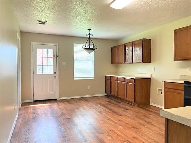 714 Kinston Ct, Wylie, TX 75098 - kitchen featuring light wood finished floors, hanging light fixtures, a textured ceiling, baseboards, and light countertops
