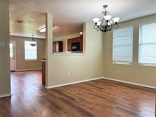 714 Kinston Ct, Wylie, TX 75098 - unfurnished dining area with dark wood-style flooring, a textured ceiling, a notable chandelier, and baseboards