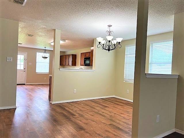 714 Kinston Ct, Wylie, TX 75098 - unfurnished dining area featuring a notable chandelier, dark wood finished floors, and a textured ceiling