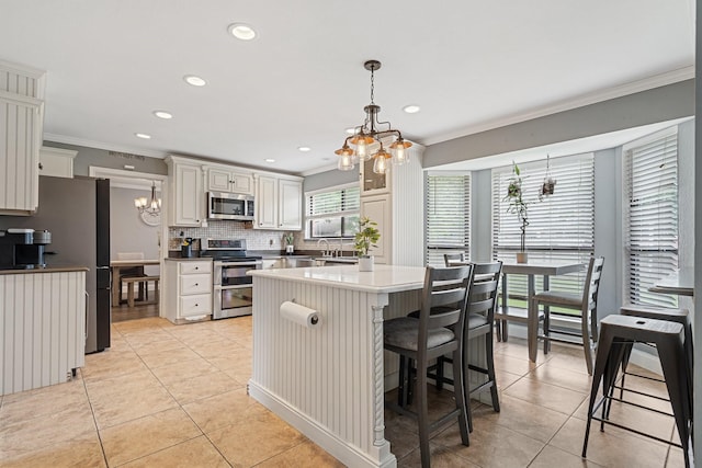 kitchen with appliances with stainless steel finishes, light tile patterned floors, ornamental molding, and a notable chandelier