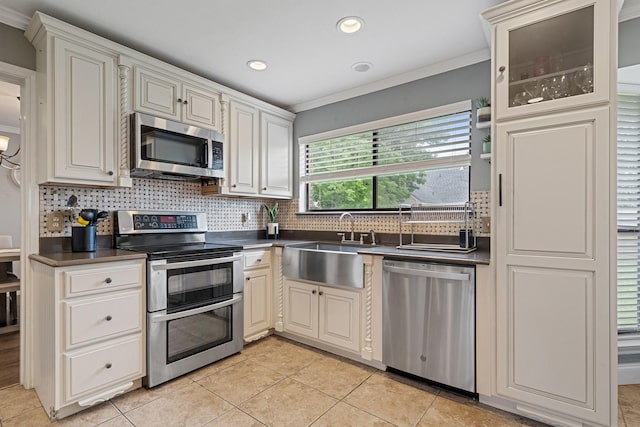 kitchen with ornamental molding, a sink, dark countertops, tasteful backsplash, and appliances with stainless steel finishes