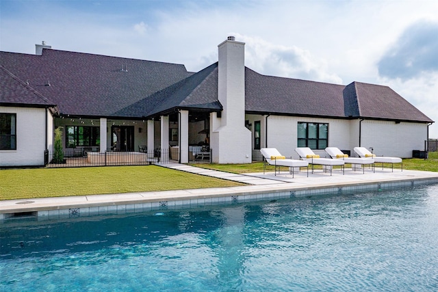 rear view of house featuring a chimney, a lawn, a shingled roof, a patio area, and an outdoor pool