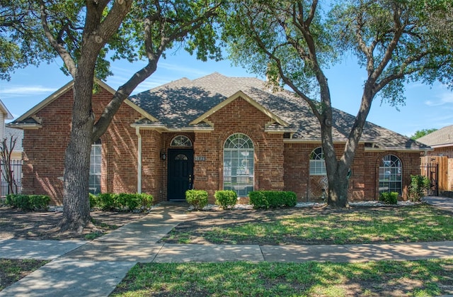 view of front of property with brick siding, a shingled roof, and fence