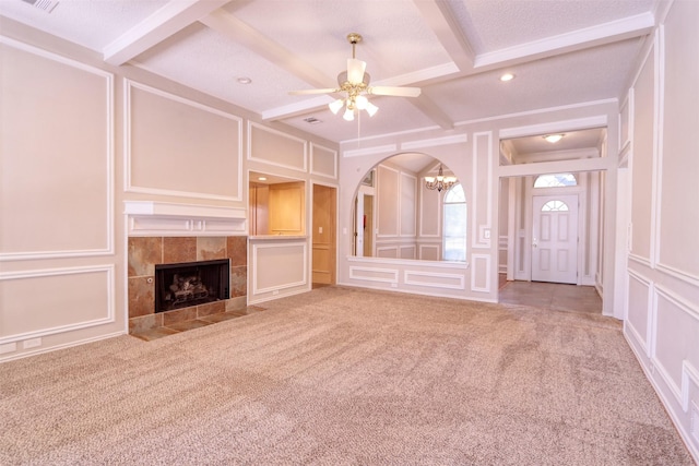 unfurnished living room with a tiled fireplace, a decorative wall, beam ceiling, and carpet floors