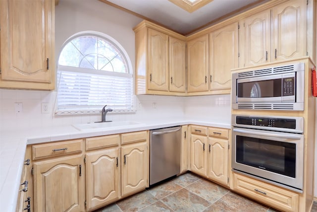 kitchen with appliances with stainless steel finishes, light brown cabinetry, tasteful backsplash, and a sink