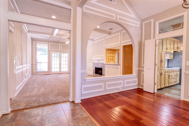 unfurnished living room featuring lofted ceiling with beams, a decorative wall, visible vents, ceiling fan, and arched walkways