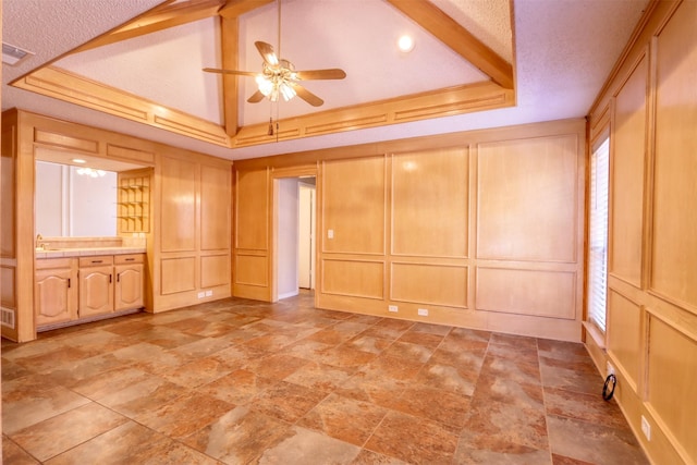 empty room featuring a tray ceiling, ceiling fan, a decorative wall, and stone finish floor