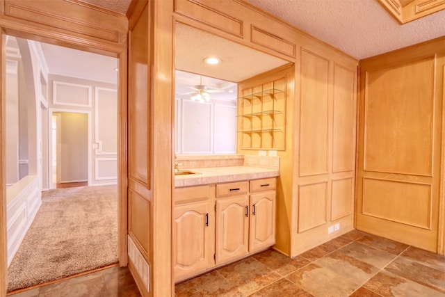interior space featuring a ceiling fan, a decorative wall, vanity, and a textured ceiling
