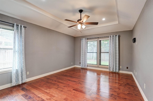 spare room featuring a raised ceiling, wood finished floors, ceiling fan, and baseboards