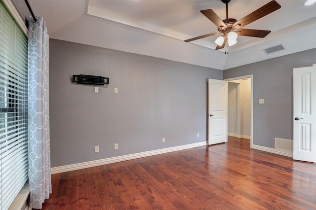 unfurnished bedroom featuring a raised ceiling, wood finished floors, baseboards, and a ceiling fan