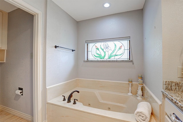 full bath with a tub with jets, vanity, and baseboards