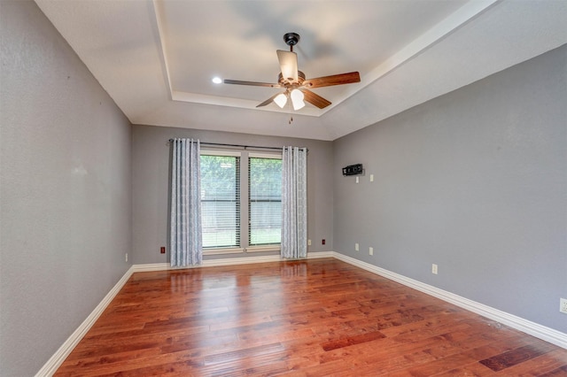 spare room featuring a tray ceiling, ceiling fan, wood finished floors, and baseboards