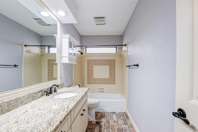 bathroom featuring toilet, baseboards, stone tile flooring, vanity, and shower / washtub combination