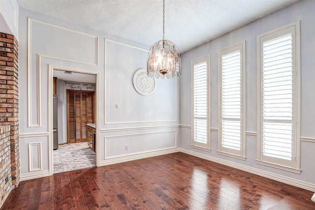 unfurnished dining area with dark wood-type flooring, a chandelier, plenty of natural light, a textured ceiling, and a decorative wall