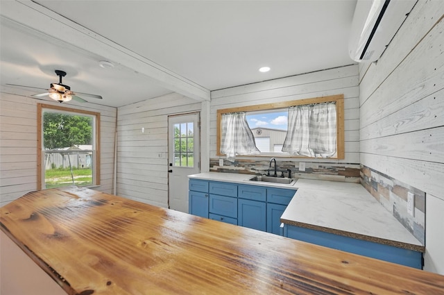 kitchen with wood counters, blue cabinetry, a sink, a wall mounted air conditioner, and wooden walls