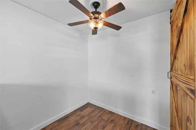 unfurnished room with a barn door, baseboards, dark wood-type flooring, and ceiling fan