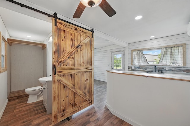 bathroom featuring a sink, wood finished floors, ceiling fan, toilet, and wooden walls