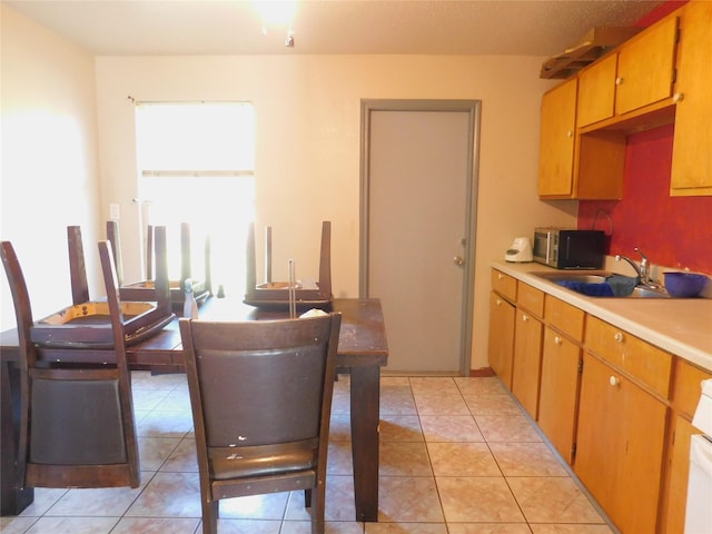 kitchen with light tile patterned floors, stainless steel microwave, light countertops, and a sink