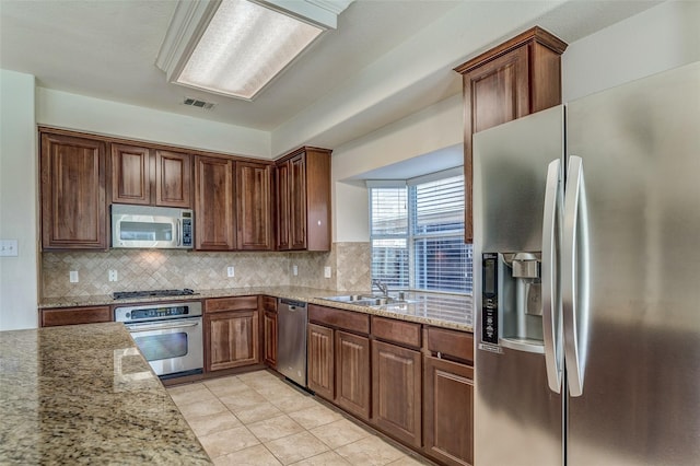 kitchen with a sink, visible vents, backsplash, light stone countertops, and appliances with stainless steel finishes