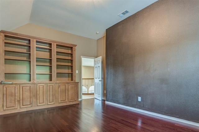 empty room featuring baseboards, dark wood-type flooring, lofted ceiling, and visible vents