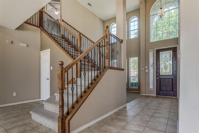foyer entrance with baseboards, a ceiling fan, visible vents, and a towering ceiling
