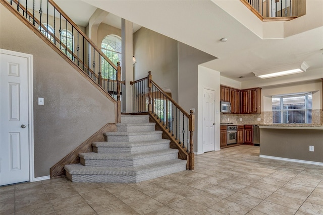 stairway with a towering ceiling, baseboards, and a healthy amount of sunlight