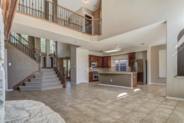 unfurnished living room featuring plenty of natural light, stairway, baseboards, and a high ceiling