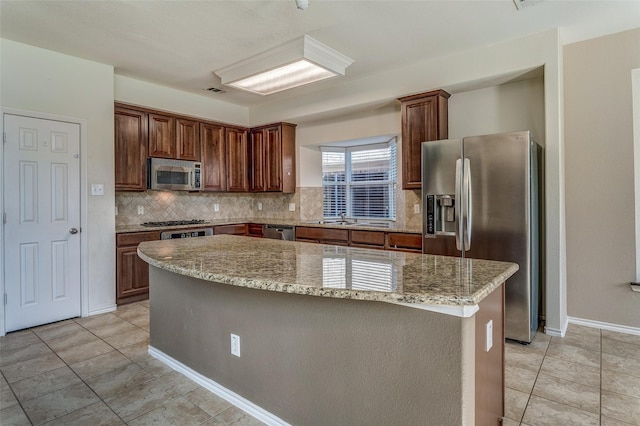kitchen with light tile patterned floors, a center island, backsplash, appliances with stainless steel finishes, and light stone counters