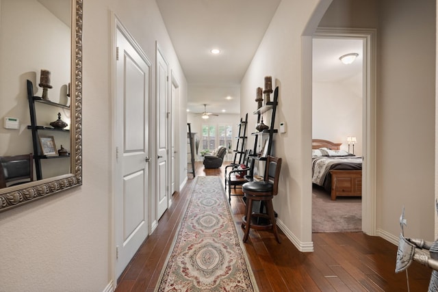 hallway featuring arched walkways, dark wood-style floors, baseboards, and recessed lighting
