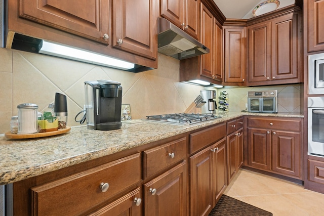 kitchen with light stone countertops, a toaster, under cabinet range hood, stainless steel appliances, and tasteful backsplash