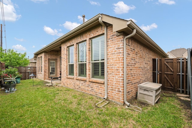 view of property exterior featuring a yard, brick siding, a fenced backyard, and a gate