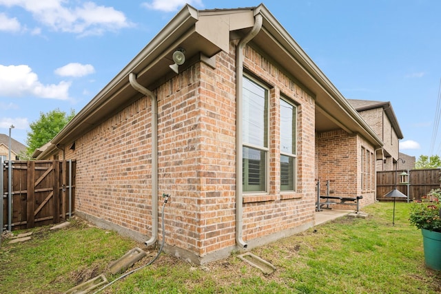 view of home's exterior with a gate, a fenced backyard, a yard, and brick siding