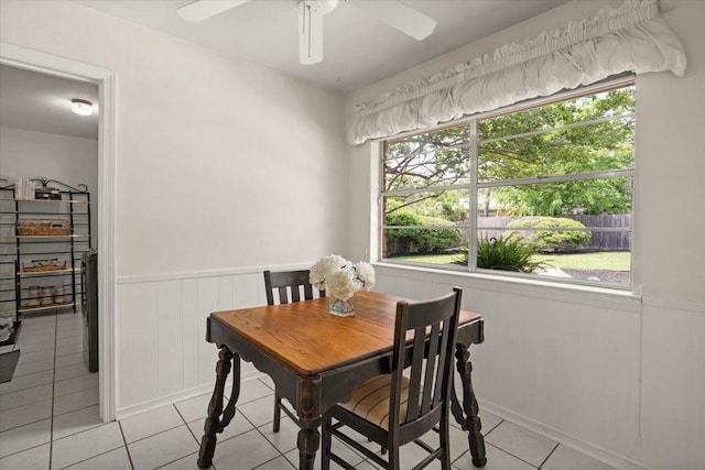 dining room with a wainscoted wall, light tile patterned flooring, and ceiling fan