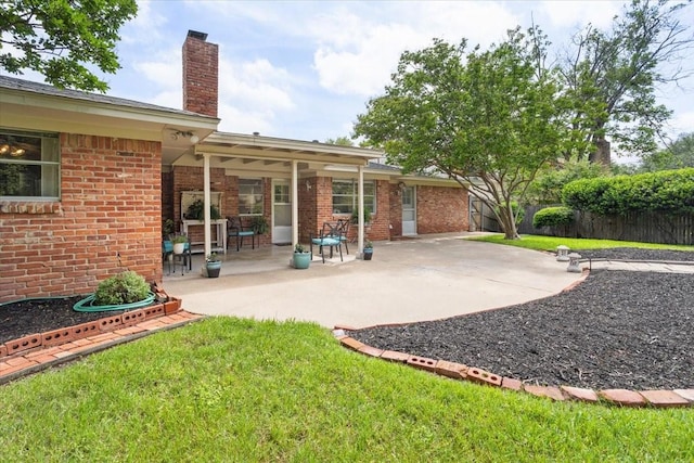 back of house with a chimney, a patio, brick siding, and a lawn