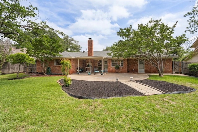 rear view of house with a patio, a chimney, a lawn, fence, and brick siding