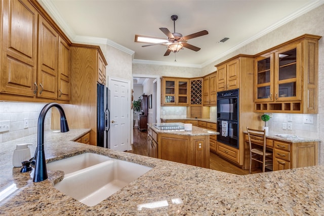 kitchen with black appliances, a sink, light stone countertops, decorative backsplash, and brown cabinets