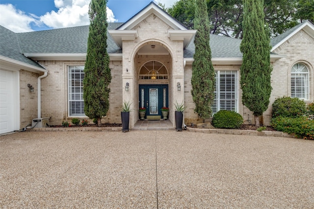 view of exterior entry featuring brick siding and a shingled roof