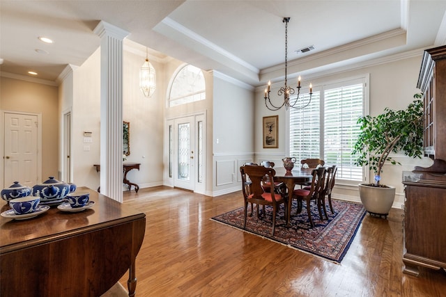 dining space with a chandelier, wood finished floors, decorative columns, ornamental molding, and a wainscoted wall