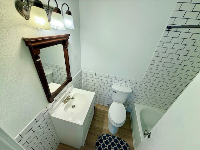 full bathroom featuring toilet, a wainscoted wall, a bathtub, tile walls, and vanity