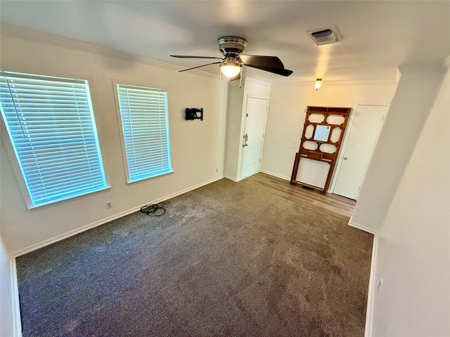 carpeted spare room with crown molding, visible vents, baseboards, and a ceiling fan