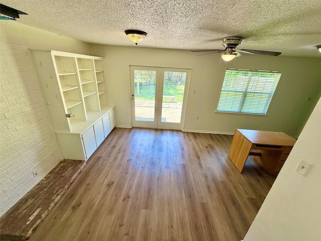 unfurnished dining area featuring a textured ceiling, a ceiling fan, brick wall, baseboards, and light wood-style floors