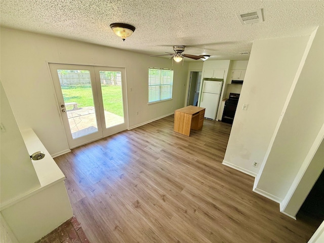 unfurnished living room with a textured ceiling, visible vents, wood finished floors, and baseboards