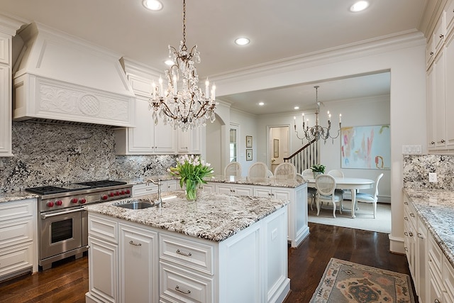 kitchen featuring a sink, a center island with sink, a chandelier, range with two ovens, and custom range hood