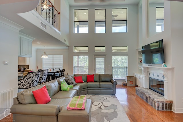 living area with light wood finished floors, a high ceiling, a glass covered fireplace, and visible vents