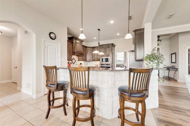 kitchen featuring a peninsula, stone countertops, baseboards, arched walkways, and appliances with stainless steel finishes