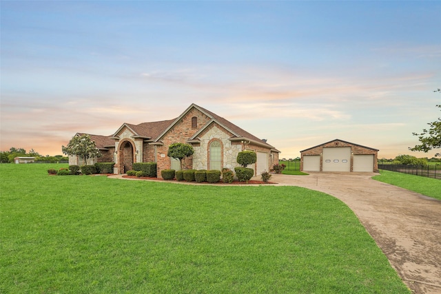 french country inspired facade with fence, stone siding, driveway, a yard, and a garage