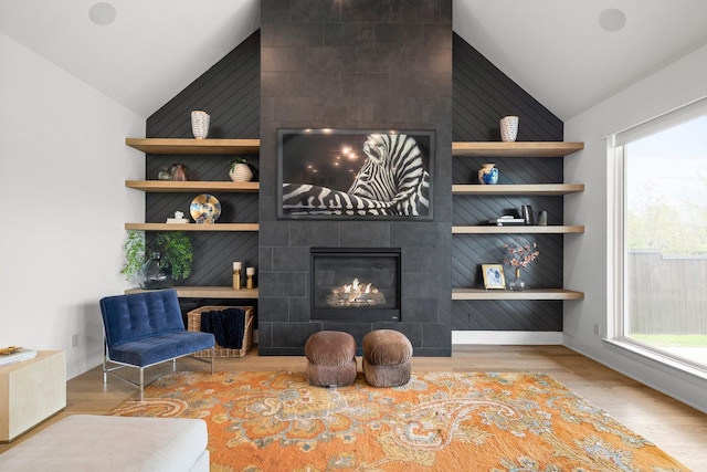 living room with vaulted ceiling, a healthy amount of sunlight, a tiled fireplace, and wood finished floors
