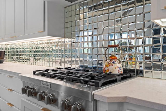 interior details with white cabinets, stove, light stone counters, and backsplash
