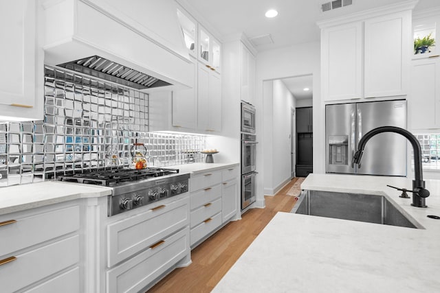 kitchen with a sink, light wood finished floors, backsplash, white cabinetry, and appliances with stainless steel finishes