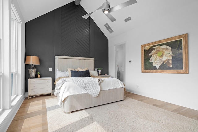 bedroom featuring light wood-type flooring, high vaulted ceiling, visible vents, an accent wall, and ceiling fan